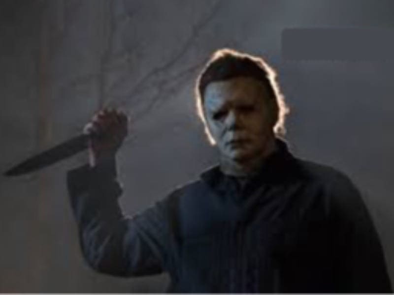 A person in a white mask and dark clothing stands at night holding a large knife raised in one hand, evoking classic Horror Movies.