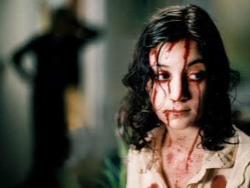 A girl with blood on her face and clothes looks away, distressed—a scene straight from 31 Days of Horror Movies. A shadowy figure stands blurred in the background.