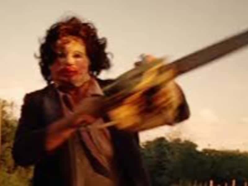 Person wearing a mask holds a chainsaw outdoors, evoking classic horror films—perfect for your 31 Days of fright. Blurred trees and sky fill the background.
