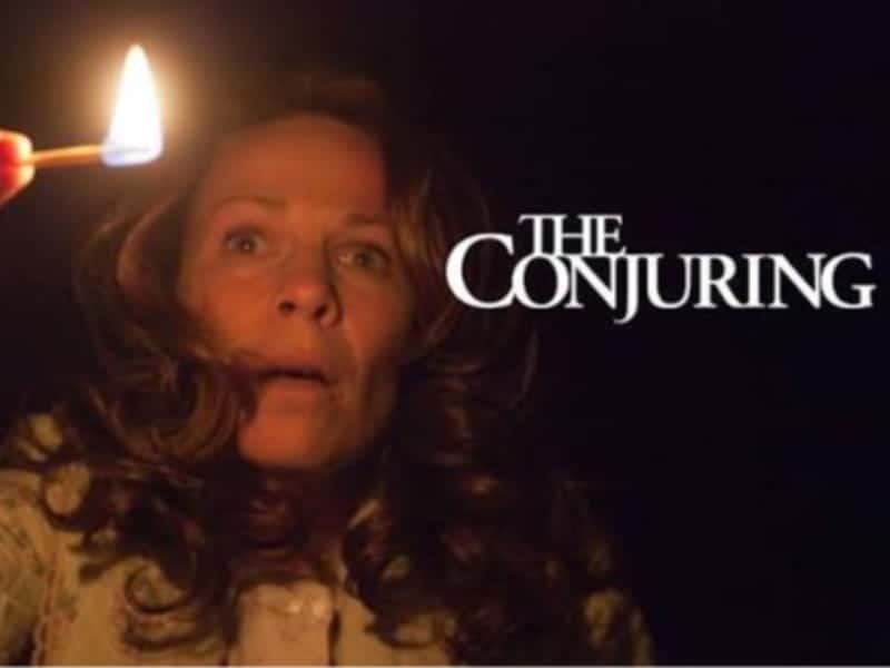 A woman holds a lit match in darkness with a startled expression. “The Conjuring” appears beside her, perfect for fans of chilling Horror Movies.