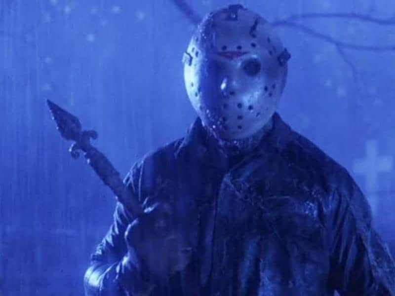 A person in a hockey mask stands in the rain at night, holding a sharp weapon, channeling classic Horror Movies with a blue-toned background.