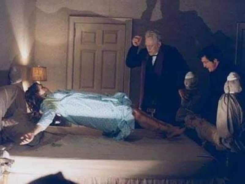 A girl in a nightgown levitates above a bed while two men stand nearby, one raising his hand—a chilling scene inspired by classic horror movies.