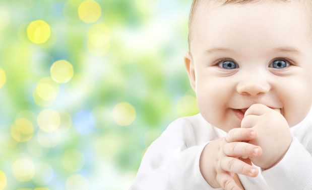 A baby is smiling in front of a green background.