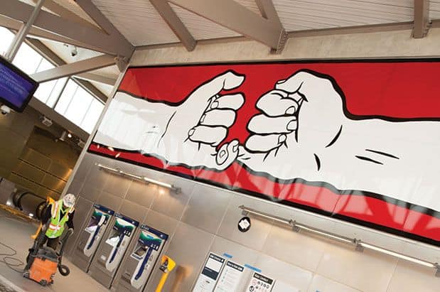 A man is painting a mural of two fists on a wall.