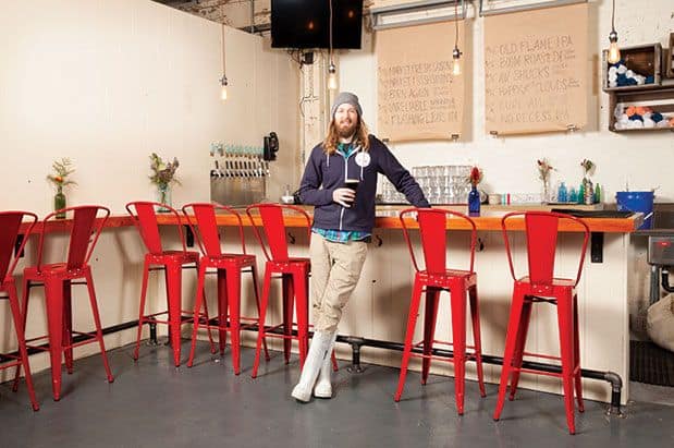 A man standing in front of a bar with red stools.