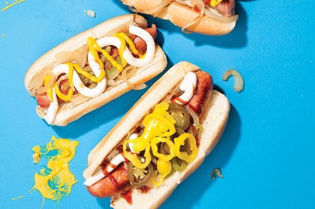 Three hot dogs with mustard and onions on a blue background.