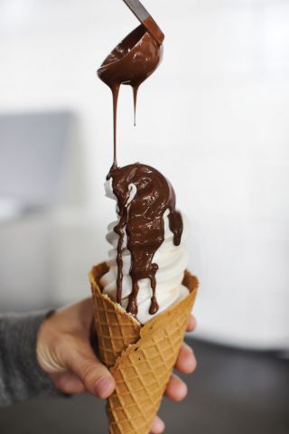 An ice cream cone with chocolate dripping over it.