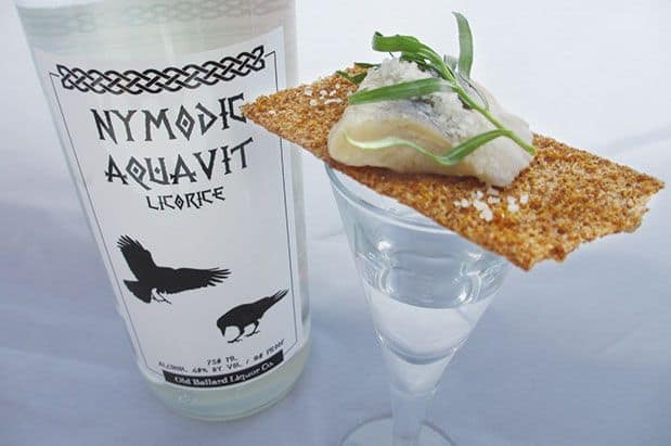 A glass with a cracker next to a bottle of aquavit.