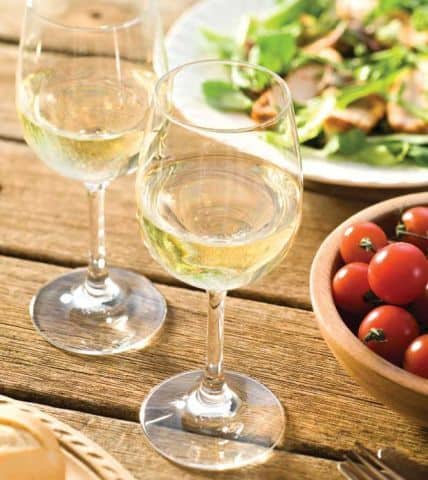 Two glasses of white wine and a salad on a wooden table.