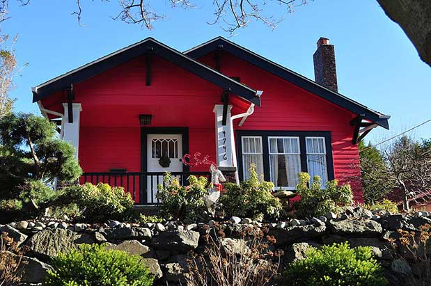 A red house with black trim and bushes.