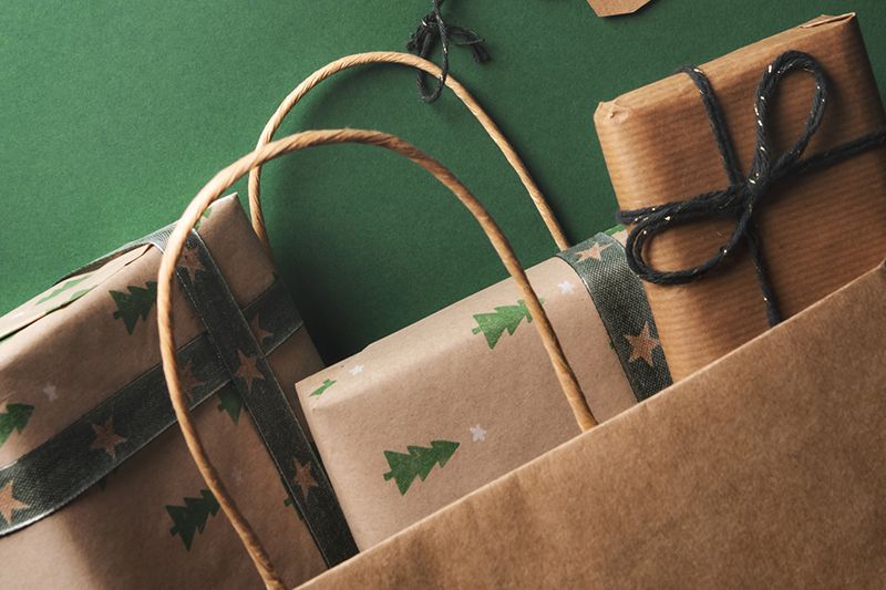 Christmas gifts, wrapped in classic brown paper, dropping from an overturned paper bag and two unwritten labels tied to the handle.