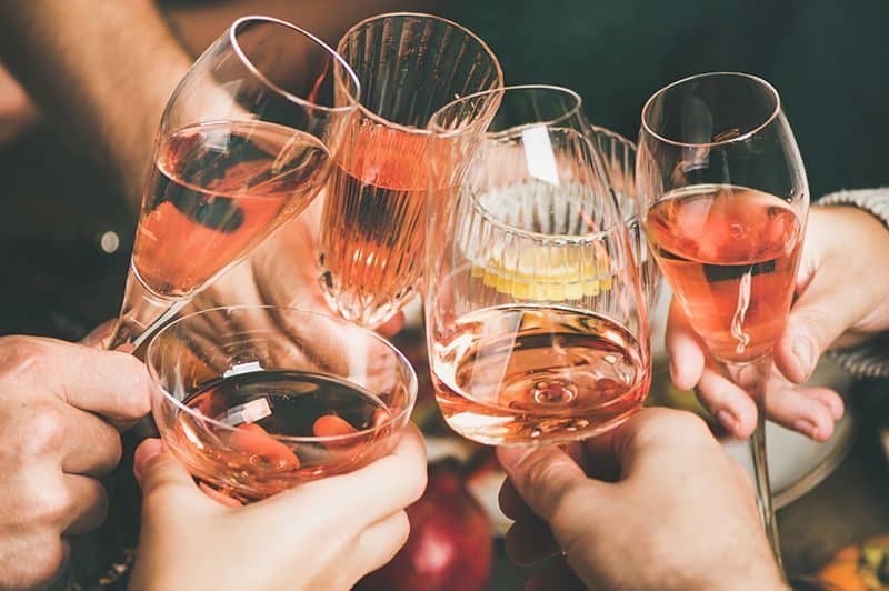 Traditional Christmas or New Year holiday celebration party. Friends or family feasting and clinking glasses with rose wine at festive Christmas table with homemade snacks, square crop