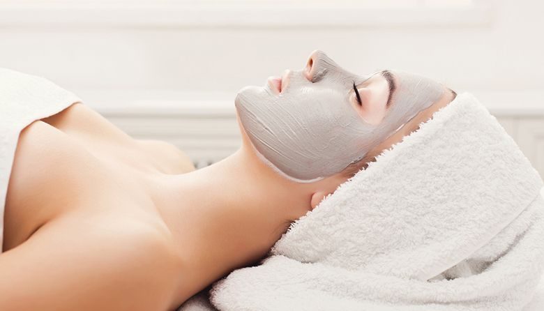 Face mask, spa beauty treatment. Woman applying facial clay mask at spa salon, skincare, side vies