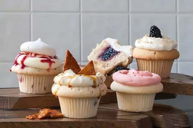 Five cupcakes are sitting on a wooden cutting board.