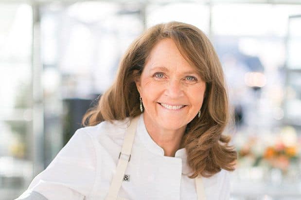 A woman in a white chef's apron smiling.