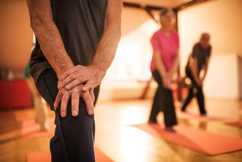 Unrecognizable senior man stretching his leg on exercise class while other seniors are in the background.