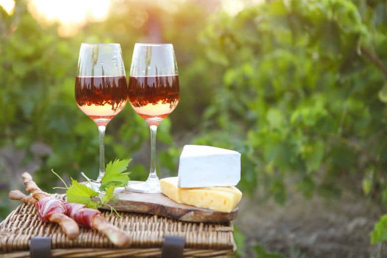 Two glasses of rose wine with bread, meat, grape and cheese on the vineyard background