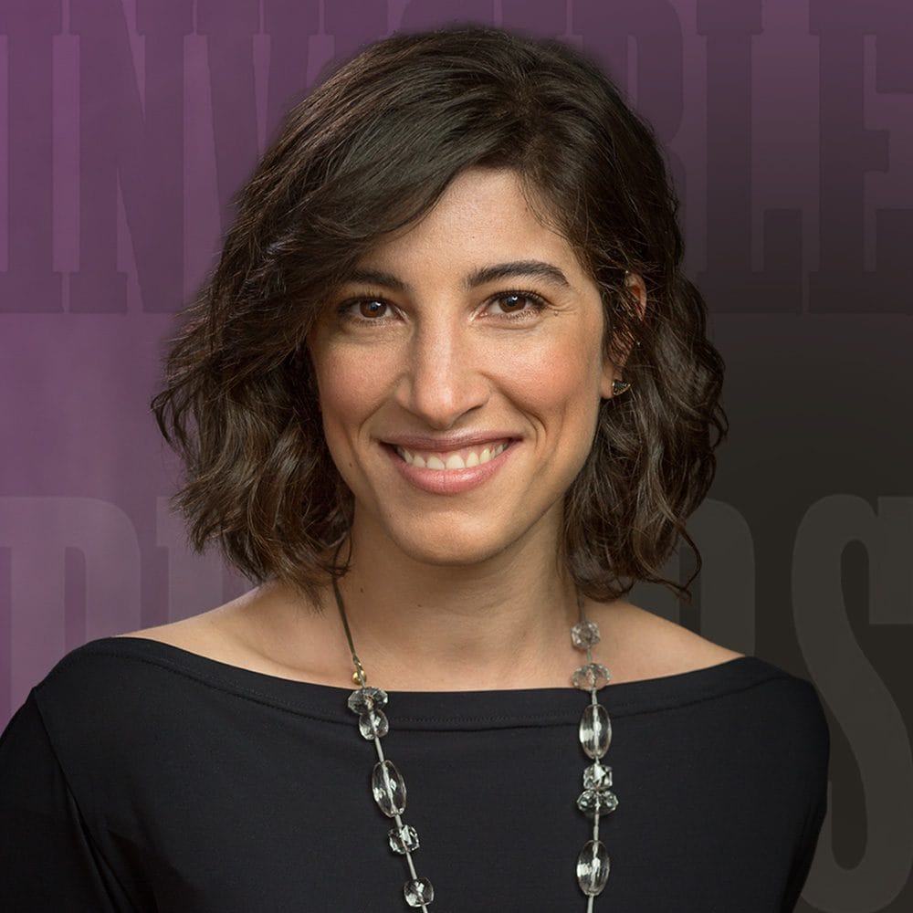 A person with short, wavy hair wearing a black top and a beaded necklace smiles at the camera against a dark, gradient background, embodying the style and confidence of the digital age.