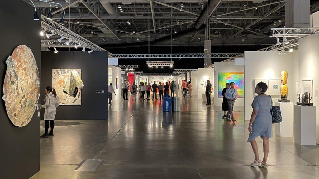 People are viewing and walking through a modern art exhibition at the Seattle Art Fair in a spacious gallery with various colorful artworks on the walls and displays, making for a strong showing.
