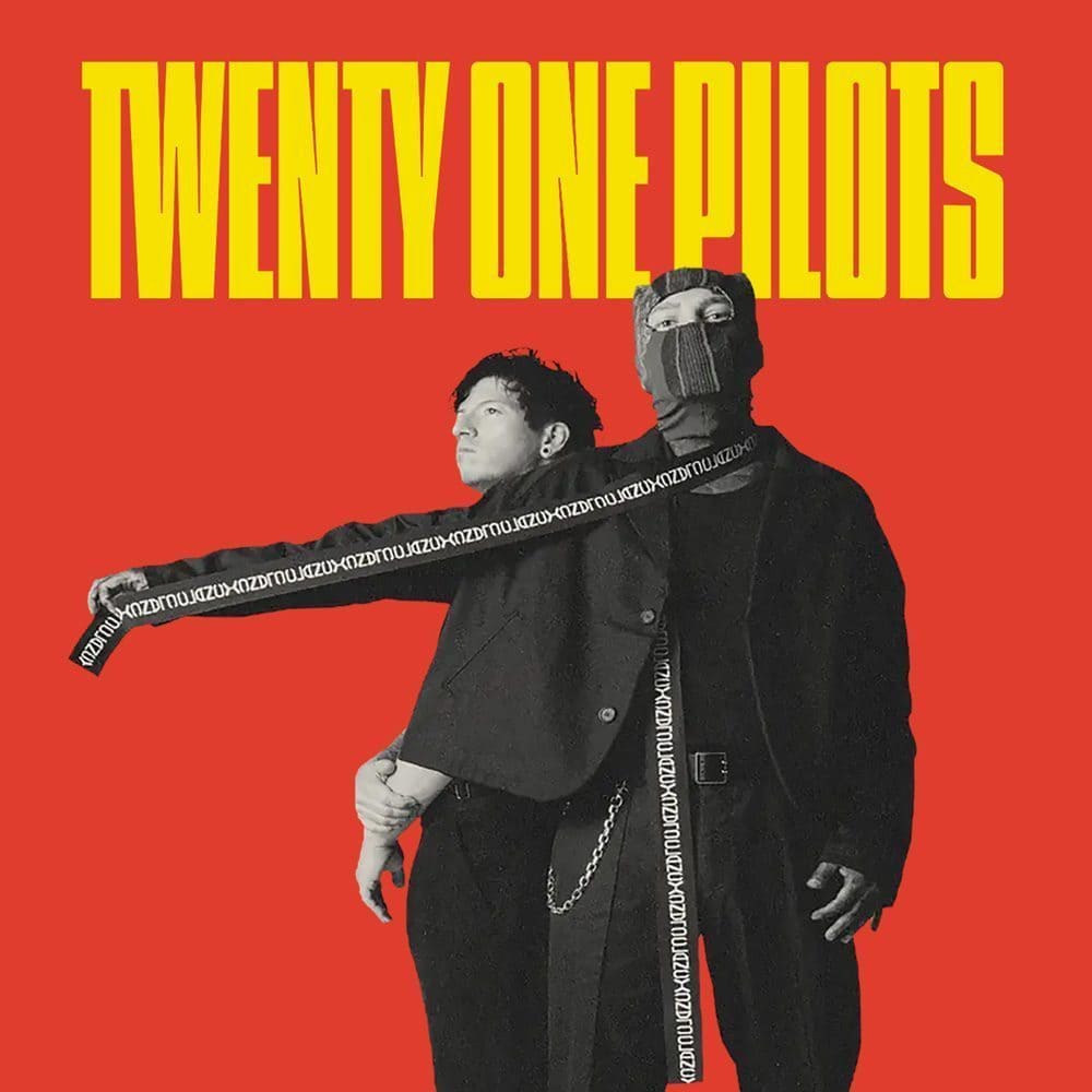 Two people stand side-by-side against a bright red background, with "TWENTY ONE PILOTS" in large yellow letters above them. One person sports a mask covering their lower face, adding an air of mystery to the dynamic duo.
