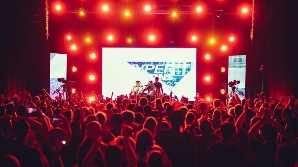 A large crowd in Seattle faces a brightly lit stage with performers and a screen displaying graphics of Mario and Pikachu, in an indoor concert venue.