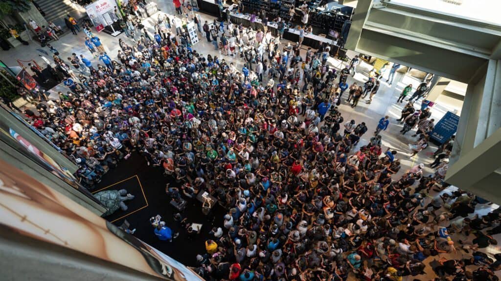 A large, diverse crowd gathers in an indoor venue for the opening of PAX West, with booths and displays visible in the background, viewed from above.