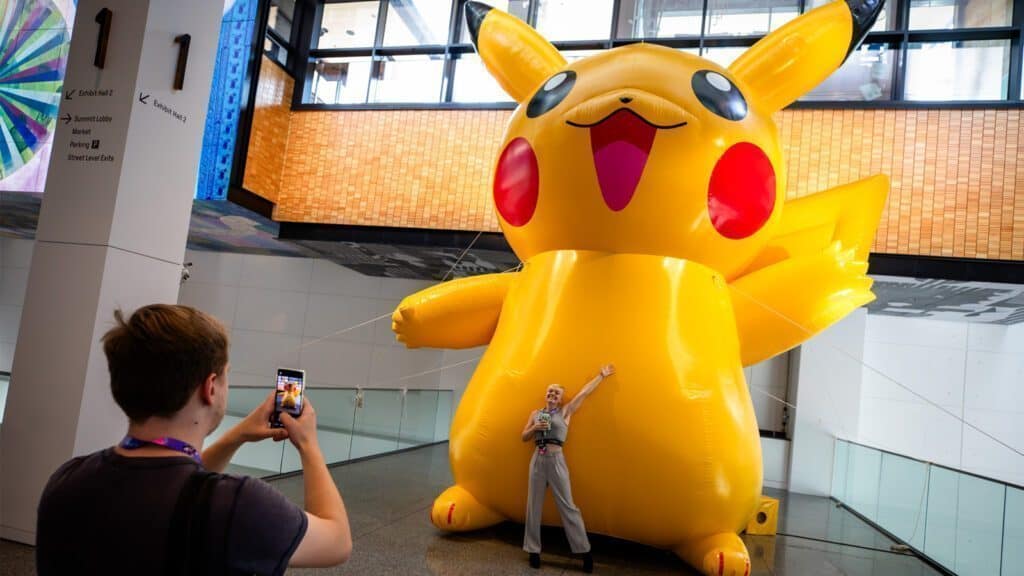 A person poses for a photo in front of a large inflatable Pikachu while another individual takes the picture using a smartphone. In the background, the iconic Space Needle adds a touch of Seattle's charm to the fun scene.