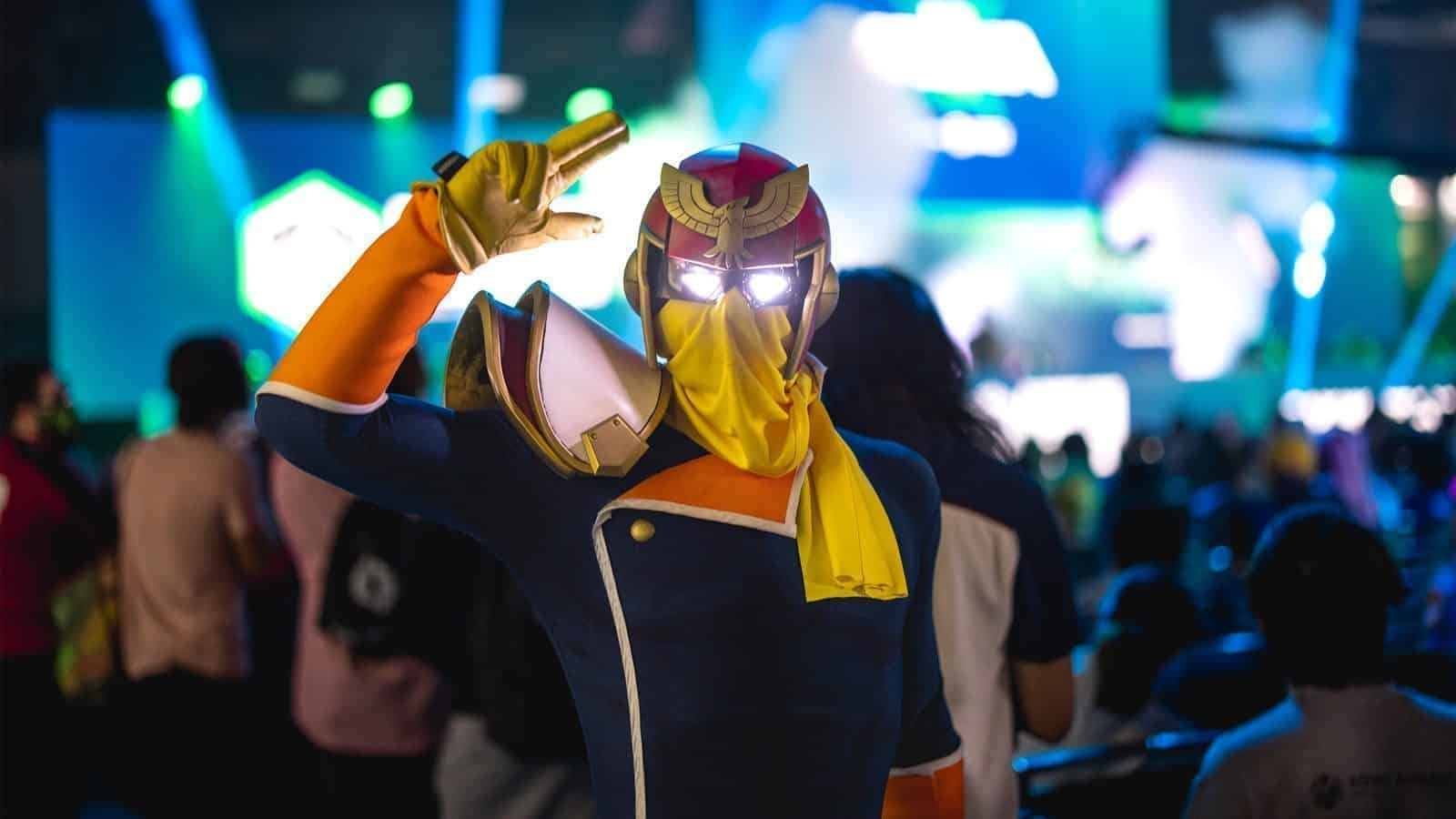 paxwest_Superhero_1600x900 A person in a colorful costume with a helmet and glowing eyes poses as Pikachu among a crowd, with a stage illuminated by green and blue lights in the background.