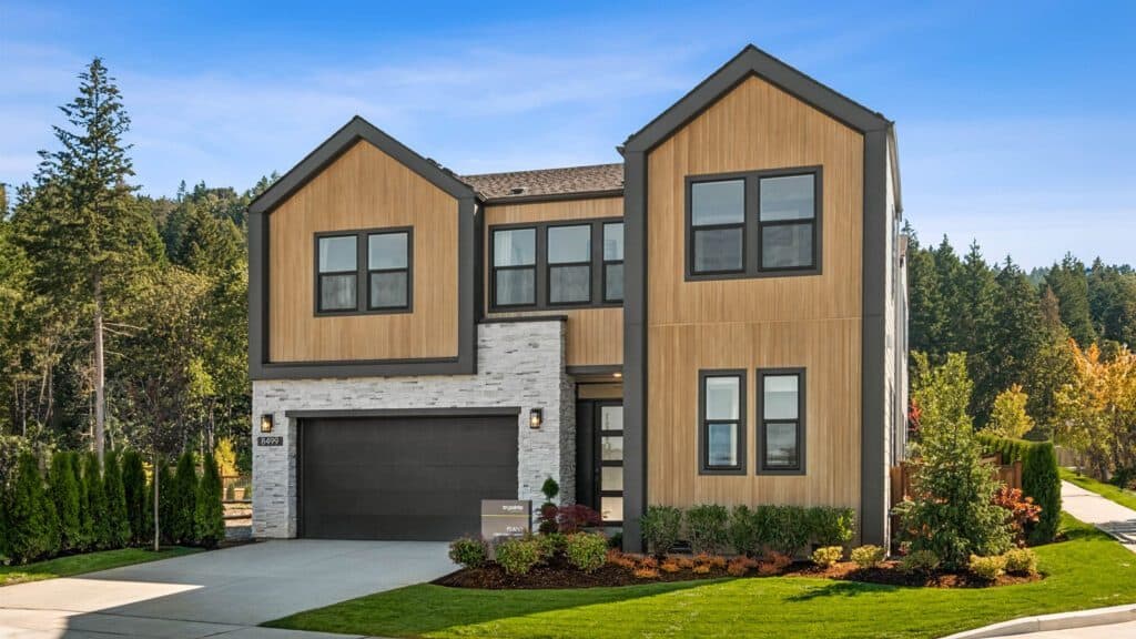 A modern two-story house in Newcastle with a wood and stone exterior, large windows, a double garage, and a well-maintained lawn. Reminiscent of Bobby Berk’s designs on Queer Eye, it's nestled in a suburban area with trees in the background.