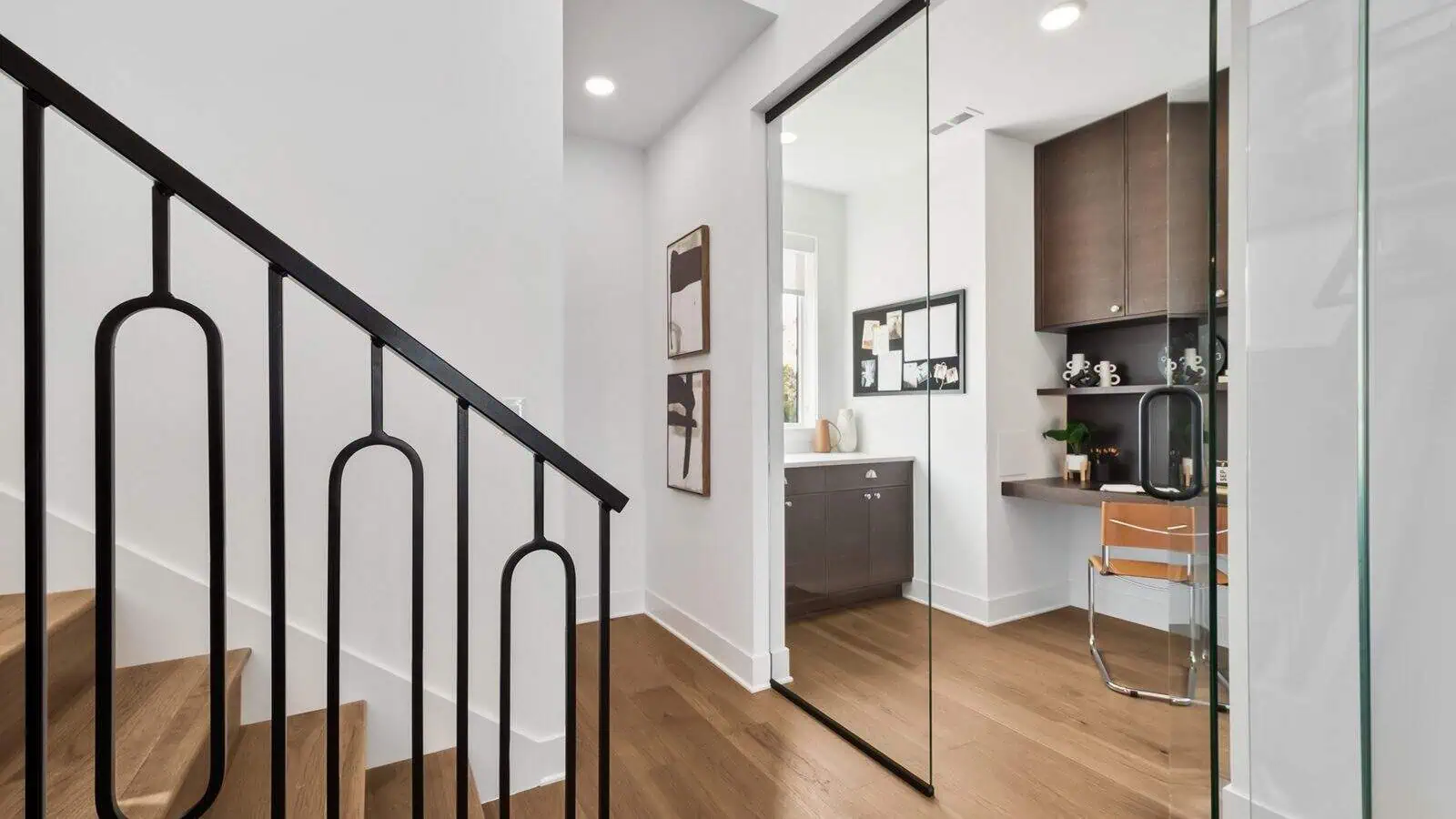 A modern residential interior designed by Bobby Berk, featuring a staircase with a black railing, a small office with a glass partition, and wooden flooring throughout the space. This Newcastle home embodies the sleek sophistication seen on Queer Eye.