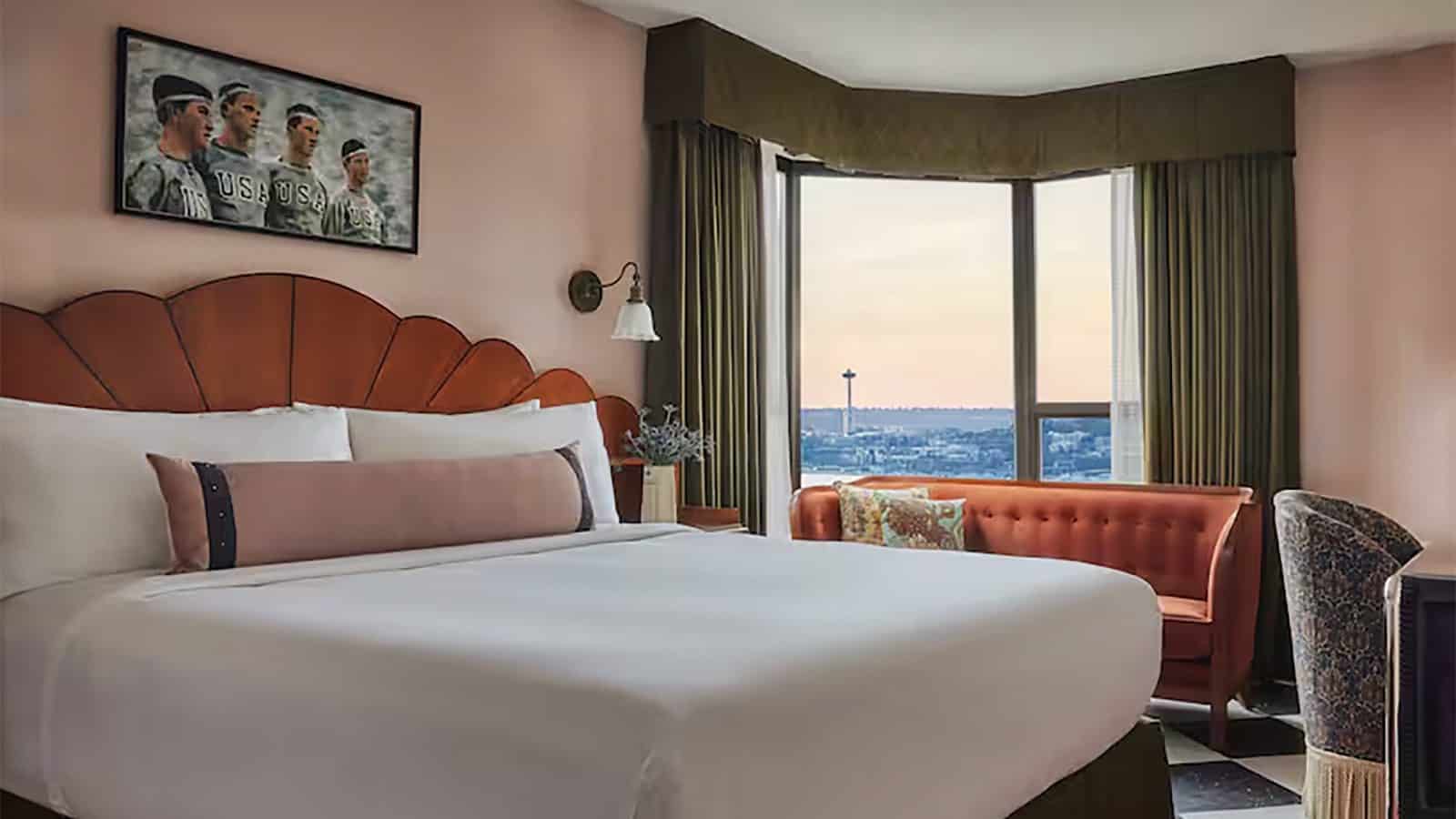 Experience the perfect staycation in our hotel room featuring a large bed, a stunning city view through a bay window, and a vintage photo on the wall. Relax on the couch by the window with a small table nearby for your convenience.
