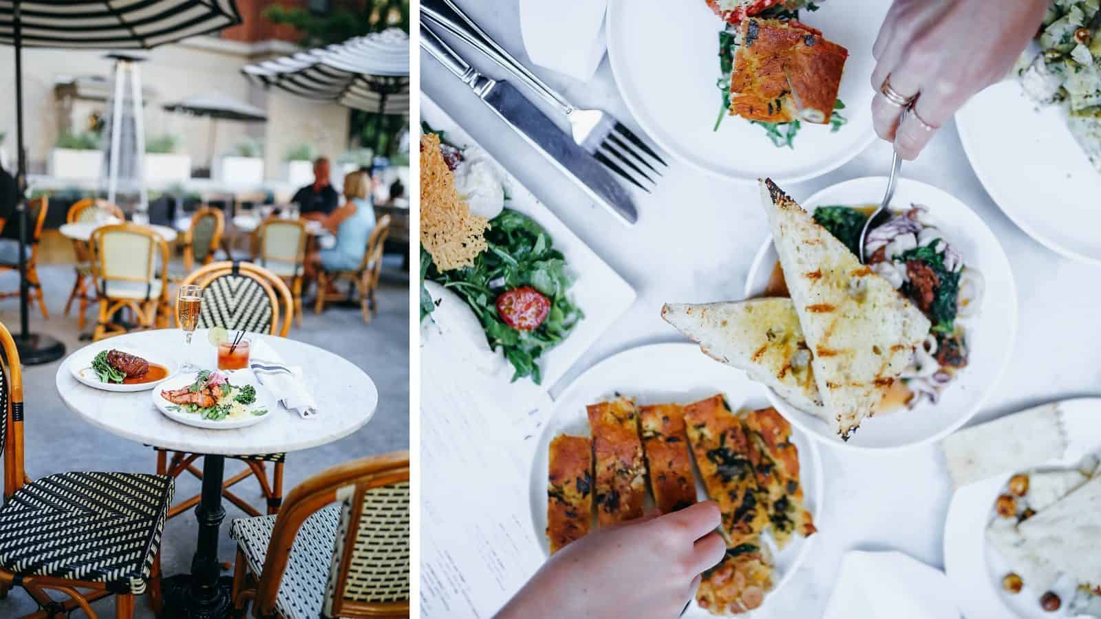 An outdoor restaurant table set for an idyllic staycation experience, featuring two dishes and a drink on one side; two hands sharing bread with various dishes on the other side.