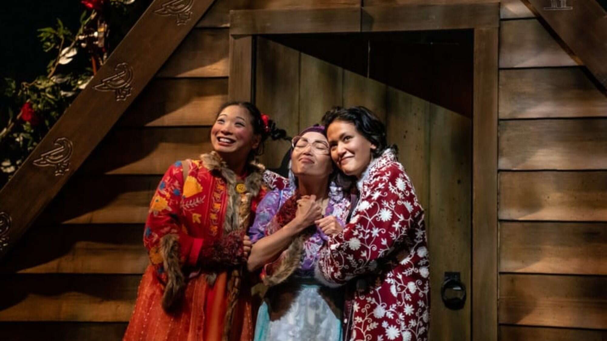 750x500_SCT_SQ24_2-16-9-2000x1125 Three people in colorful clothing stand close together, smiling and embracing in front of a wooden building—a perfect capture of friendship and joy in Seattle this week.