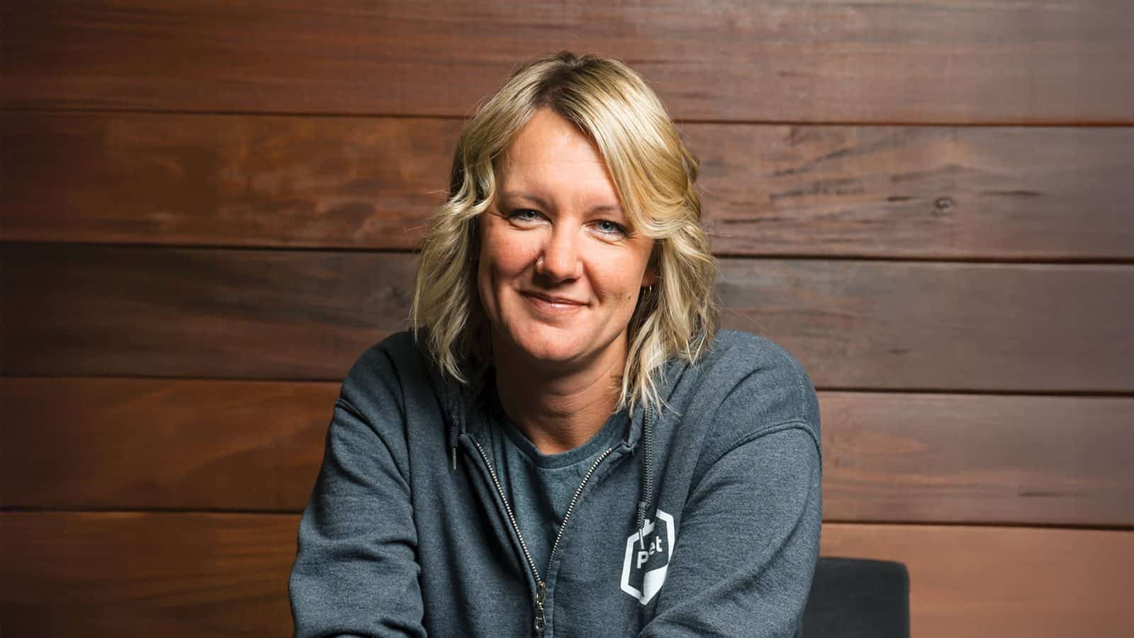 AmyKing_1600x900 A person with blonde hair in a gray hoodie smiles in front of a wooden background.