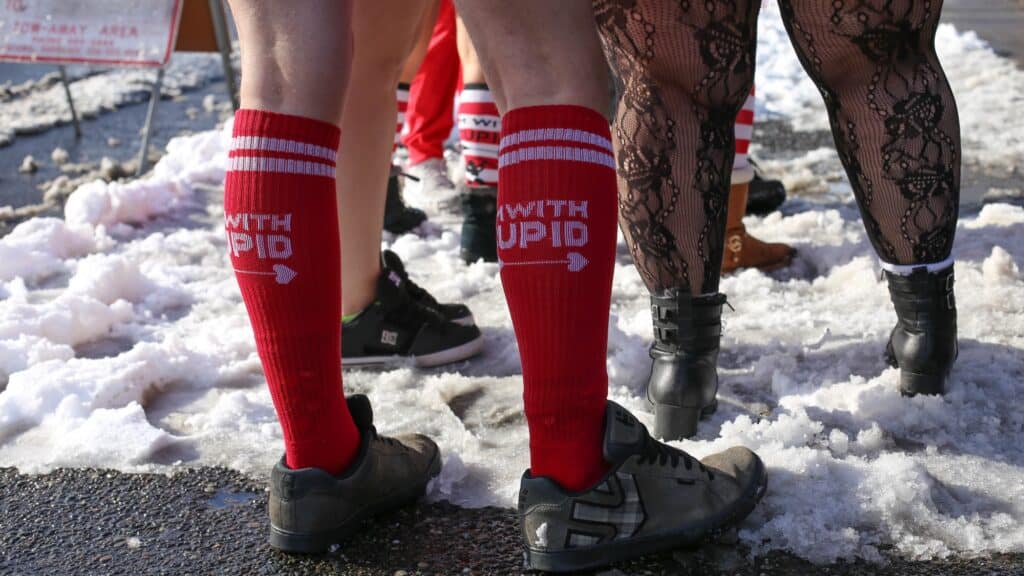 In the midst of a snow background, people stand in sports live leggings and socks. One person's red socks boldly declare "With stupid." This bizarre group seems to cover the motto, "Lost pants," As they enjoy their colorful, carefree clothing.