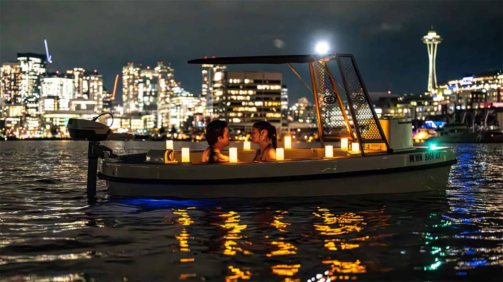 A small boat with two people on board, lit by candles, sails quietly at a city port at night. The City Skyline and Tower lights provide a romantic background, reminiscent of Valentine's magic. How much an apartment is to share such an intimate moment under the stars.