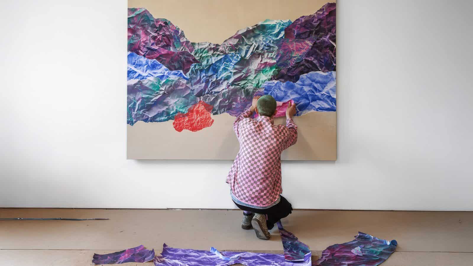 In a checkered shirt and surrounded by the vibrant energy of fresh ideas, a person assembles an abstract collage. Crumpled paper pieces lie at their feet like remnants of creativity unleashed, hinting at art as dynamic as the new hotels set to open in 2025.
