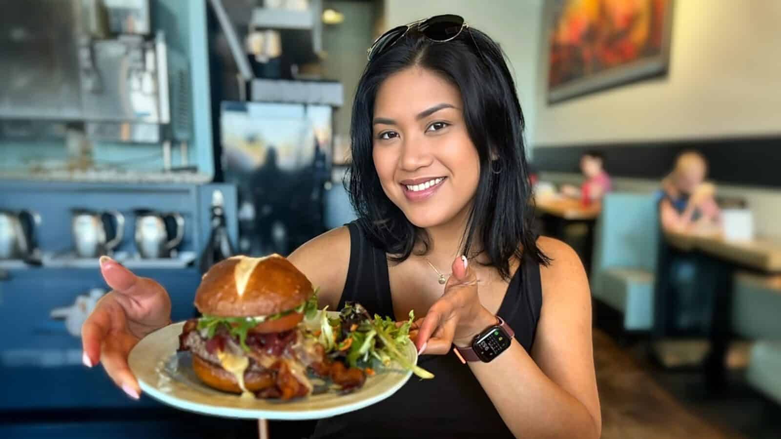Amidst the buzz of Feast Fest, a person beams while holding a plate with a burger and salad, embodying the joy of Seattle Restaurant Week on March 30.