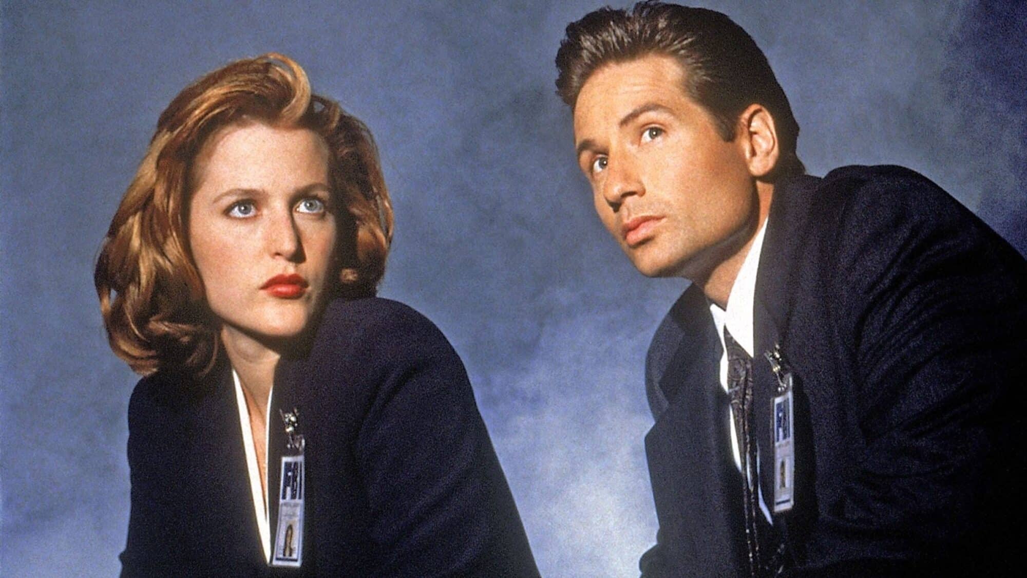 Two individuals in suits, each wearing an FBI badge, look to the side against a neutral background.