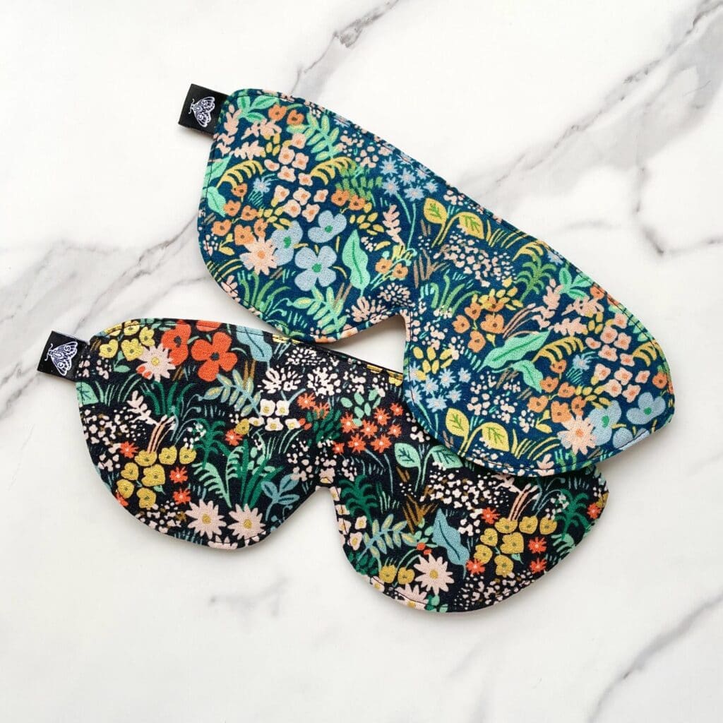 Two eye masks with colorful floral patterns are placed on a white marble surface.