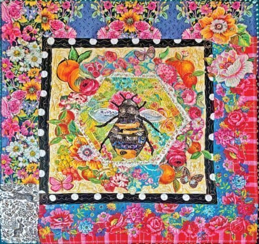 A vibrant, floral quilt features a large bee at the center, surrounded by colorful flowers, fruits, butterflies, and patterned borders—an ideal Mother's Day gift or a highlight from the Camano Island Studio Tour.