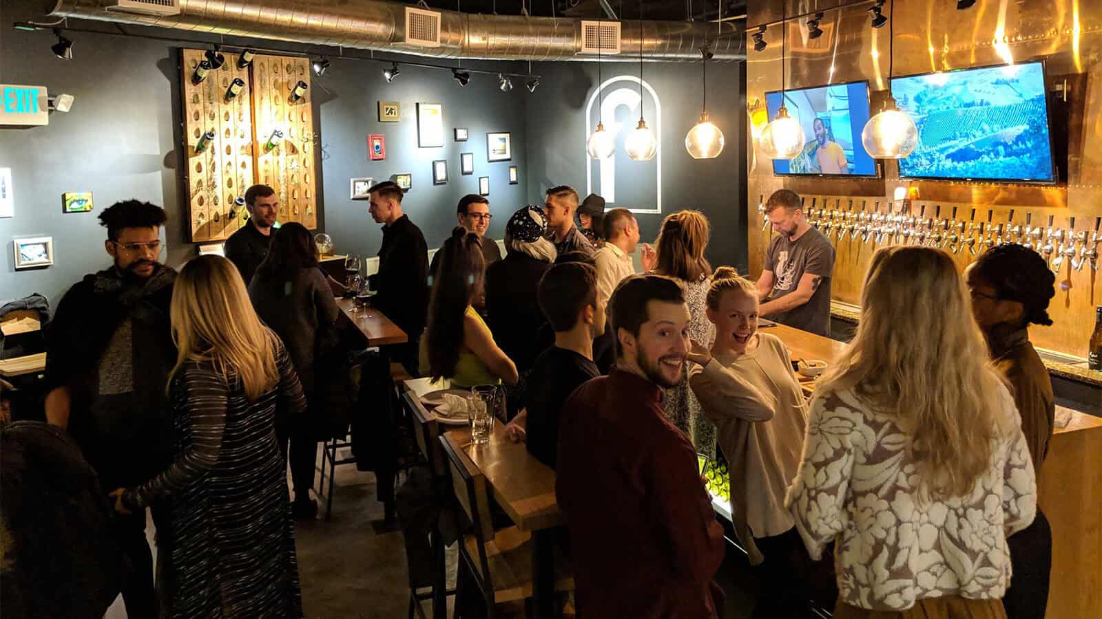 People socializing in a dimly lit bar with wall art celebrating Earth Day, a large selection of taps, and two TV screens. The atmosphere is lively and casual, underscoring the important theme of environmental awareness.