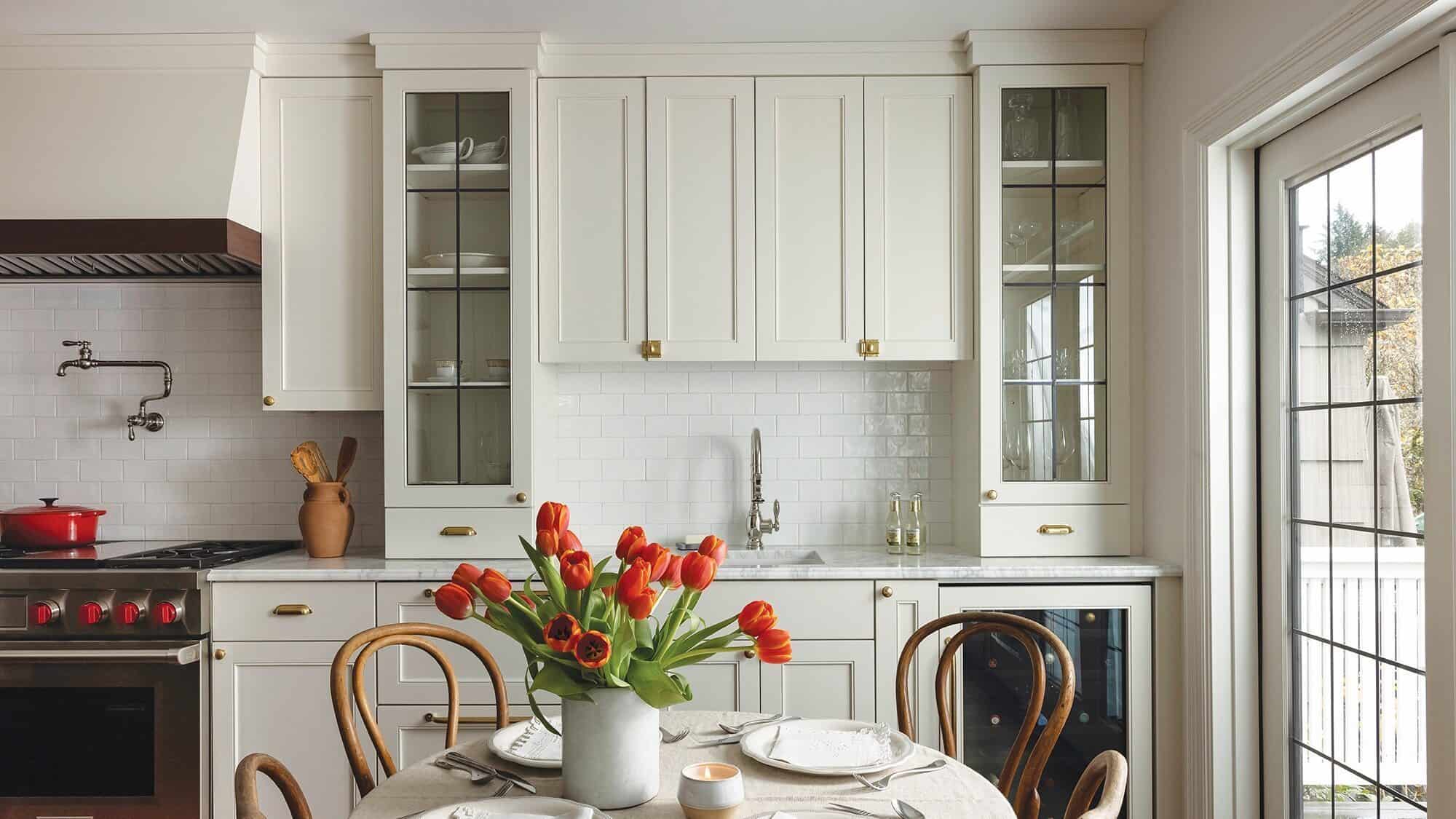 LIVING_3Z4A9202-pg-16-9-2000x1125 A bright kitchen with white cabinets, a table set for four, a vase of red tulips, and large windows letting in natural light—classic charm of living in Montlake and its historic Tudor homes.