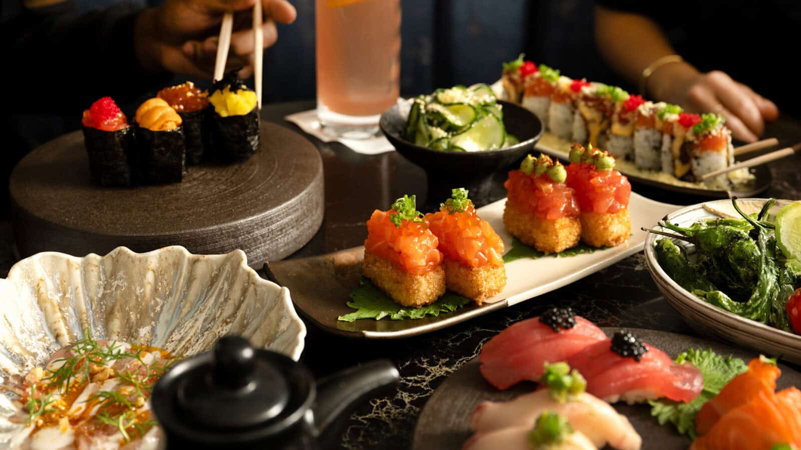 A table set with various sushi dishes, including nigiri, rolls, sashimi, cucumber salad, and a drink—like taking A Stroll Through Old & New D.C., where classic and modern flavors meet as chopsticks reach for each bite.