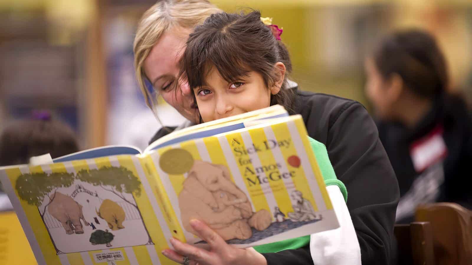 ReadingStoryBook_Credit-Kirk-Hirota_1600x900 A young girl sits on a woman's lap and reads the illustrated book "A Sick Day for Amos McGee" in a library, surrounded by stories as vital as Humanities Washington Fights ‘Midnight’ Cuts to preserve.