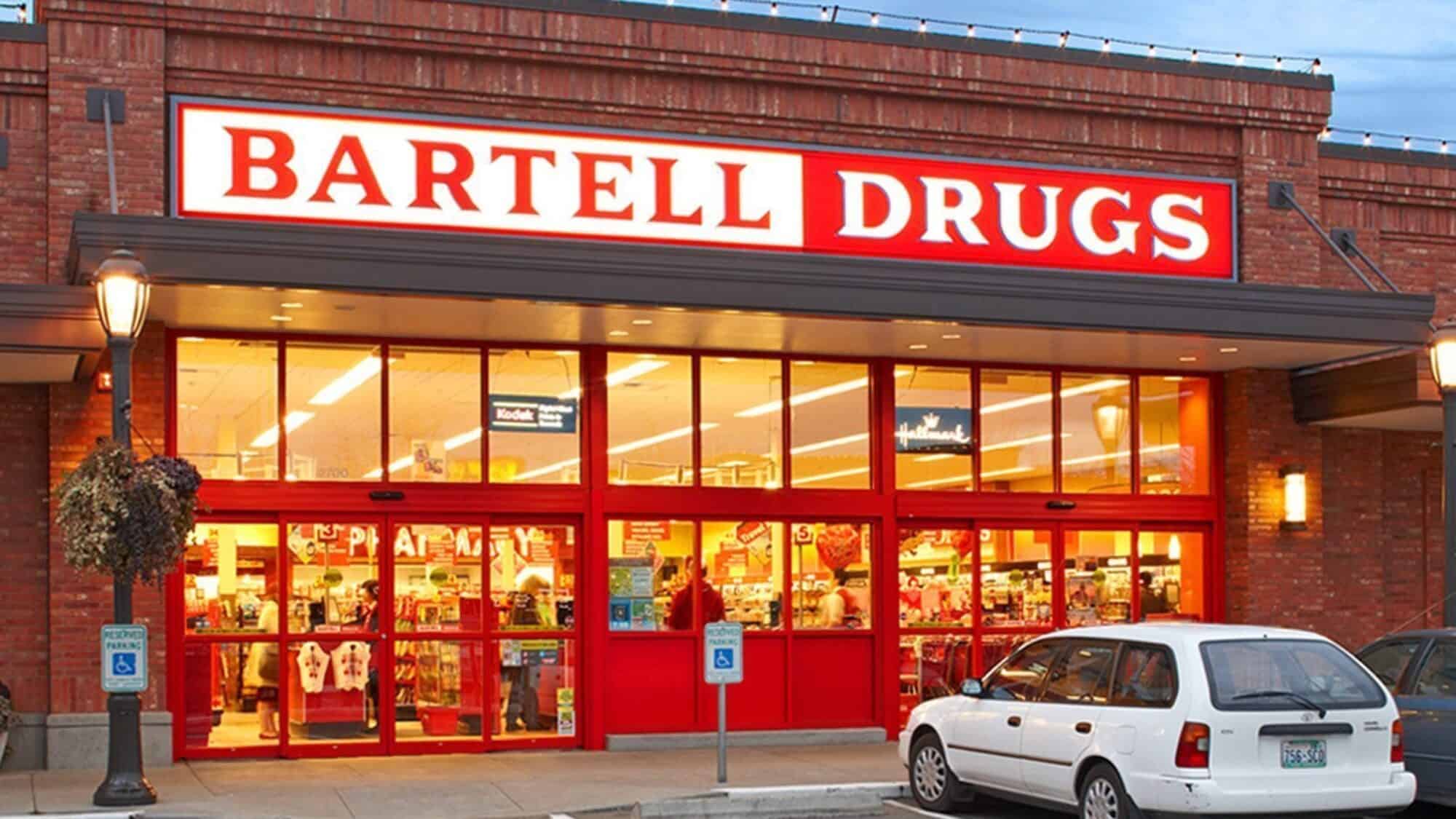 BartellDrugs-StoreFront_1800x1800-16-9-2000x1125 Exterior view of a Bartell Drugs store with bright red signage, large front windows, and a parked white car in front.