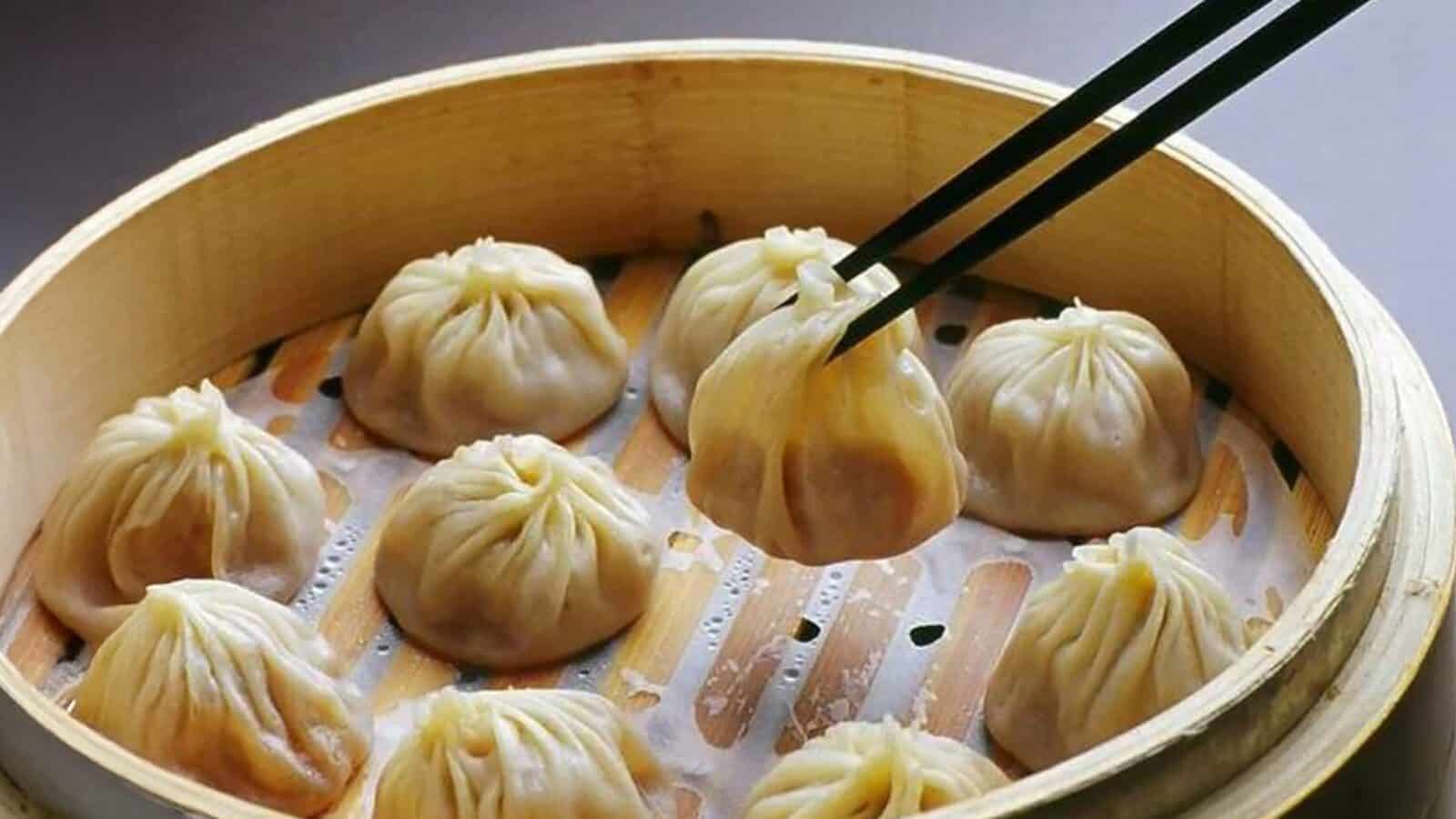 As Smoke Fades, Hope Rises in L.A.—a pair of chopsticks lifts a soup dumpling from a bamboo steamer filled with steamed delights, capturing a moment of comfort amid the city’s evolving spirit.