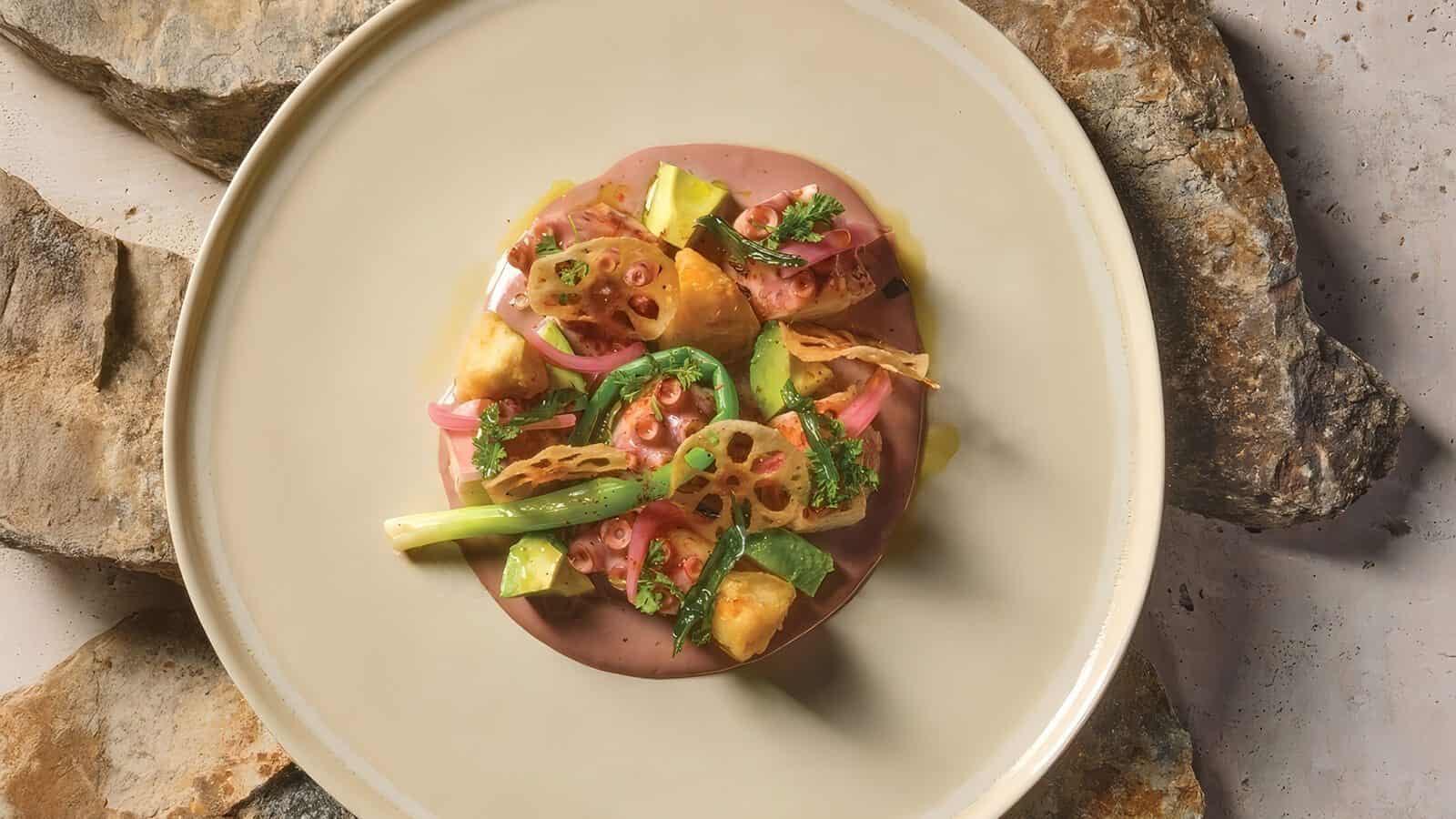 A plated dish featuring assorted vegetables, lotus root slices, greens, and sauce, arranged artfully on a beige plate placed on a stone surface—an inspiration for your next Seattle summer meal after exploring what to do in Seattle.