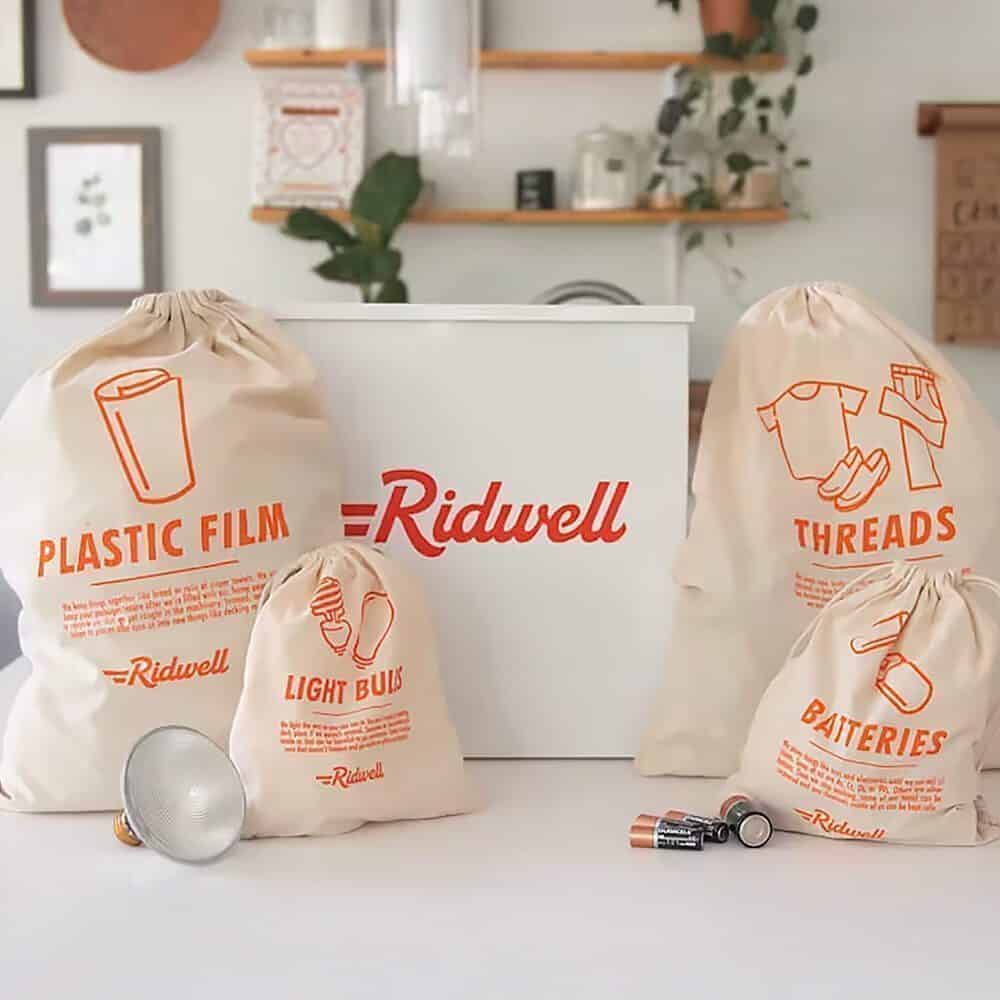 Four labeled bags for sorting recyclables—plastic film, light bulbs, threads, and batteries—are arranged in front of a white Ridwell box on a kitchen counter, making it an eco-friendly idea for your Seattle Father’s Day gift.