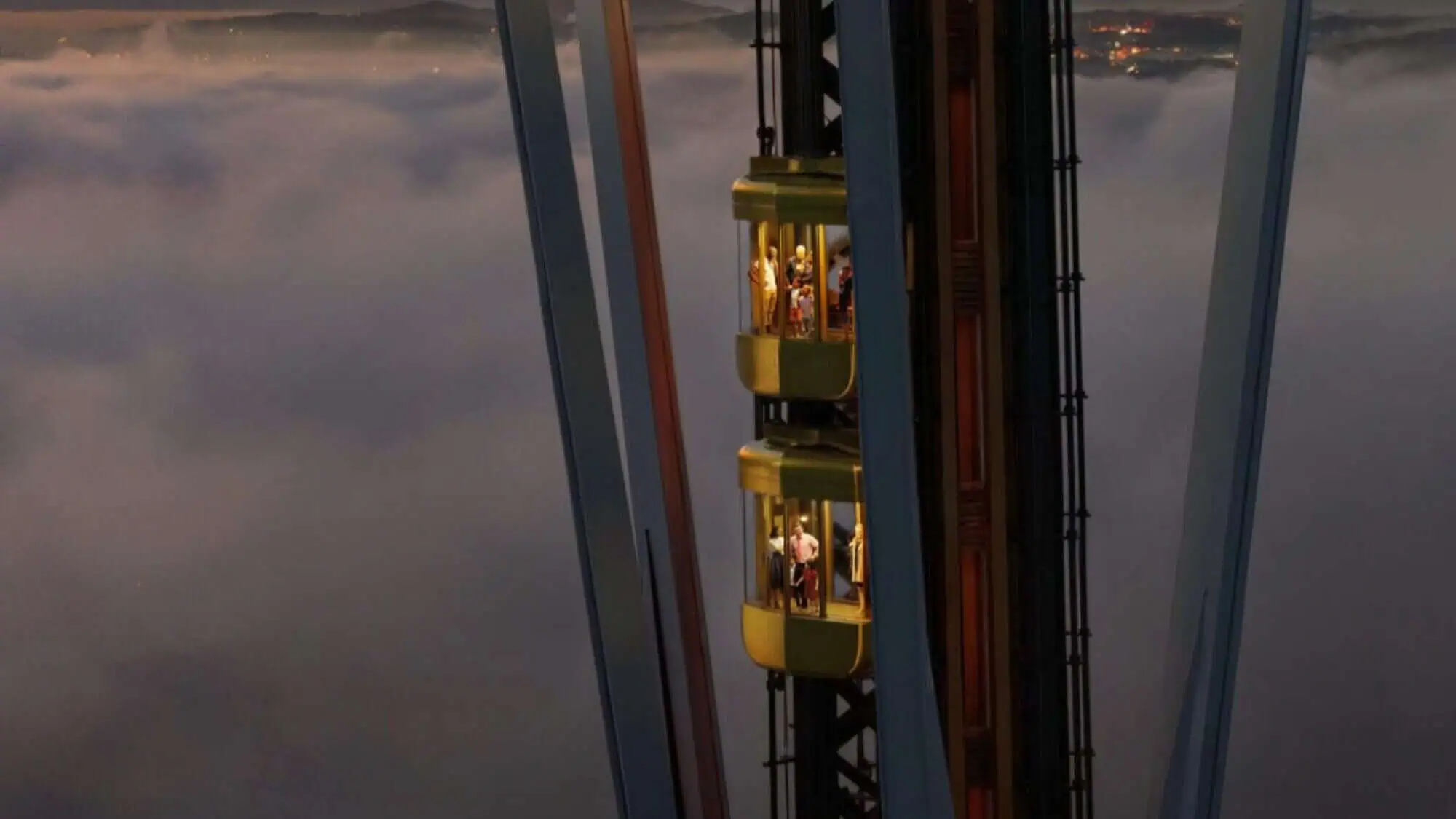SPACE NEEDLE GLASS ELEVATOR-16-9-2000x1125 Two glass elevators travel up and down a tall tower through clouds, with people visible inside looking out at the view.